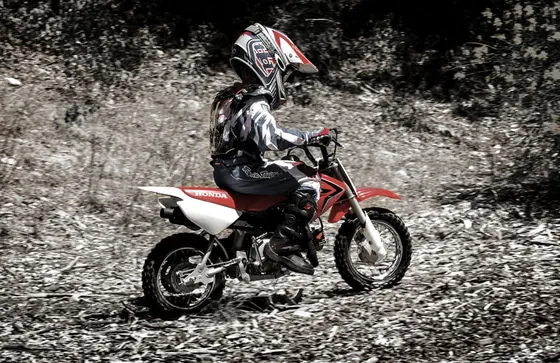 Kind mit Helm und Schutzausrüstung fährt eine Mini Motocross Honda CRF50F auf einem Waldweg